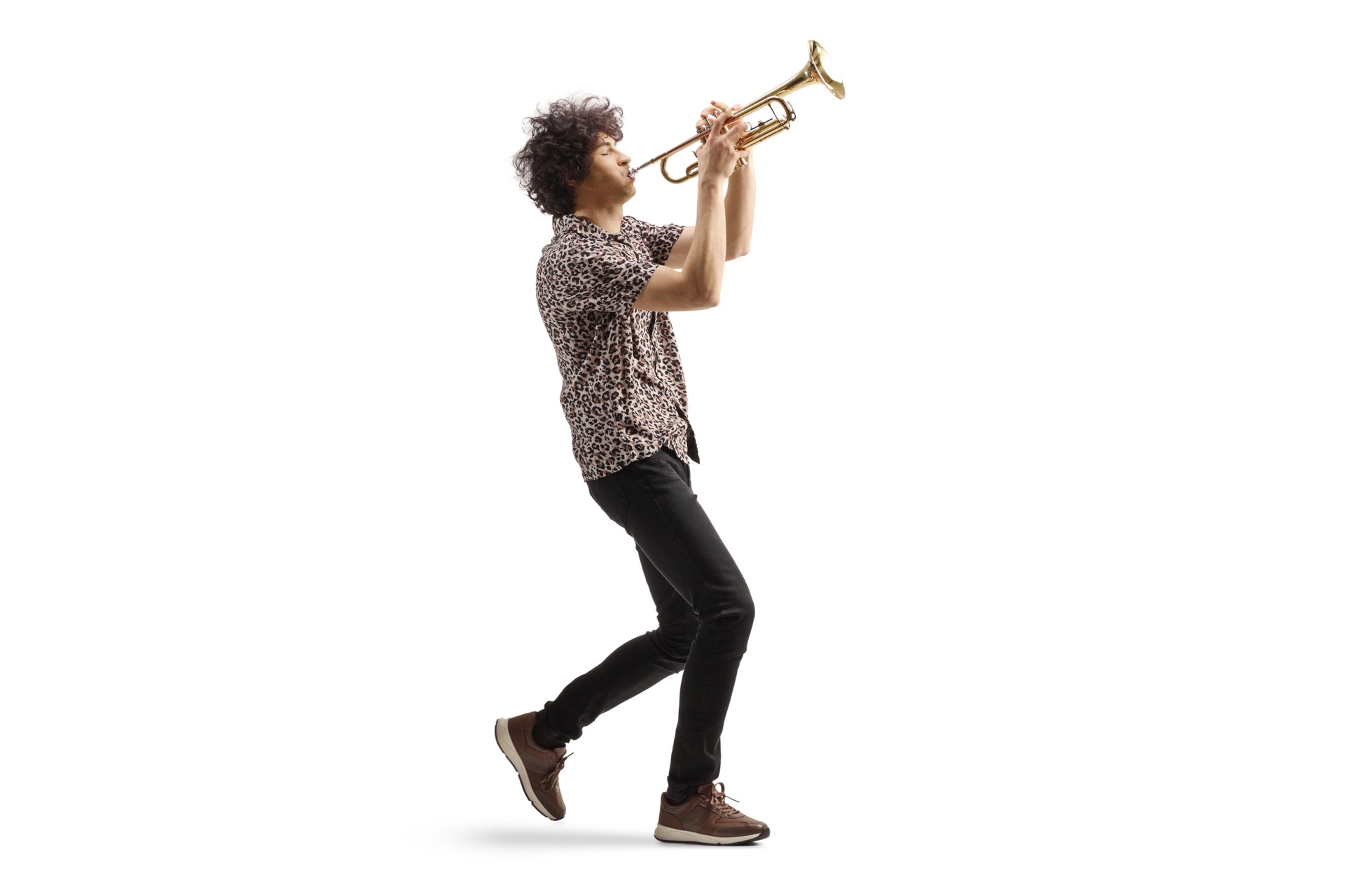 Full length profile shot of a young man walking and playing a trumpet